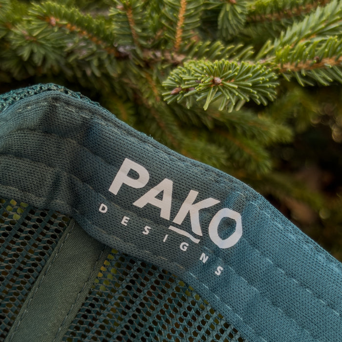 Close-up of a green fabric with 'PAKO DESIGNS' logo against a blurred green background