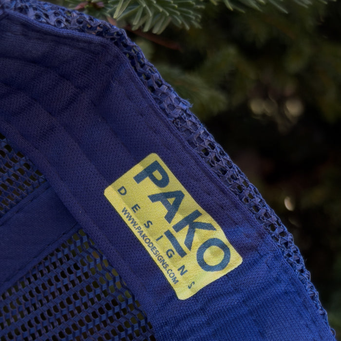 Blue fabric with a yellow 'PAKO DESIGNS' label against a blurred green background