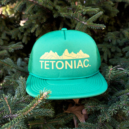 Green cap with 'TETONIAC' text and mountain design on a background of green foliage