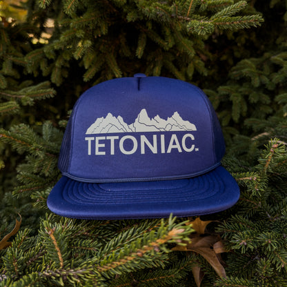 Blue cap with 'TETONIAC' logo on a background of green foliage