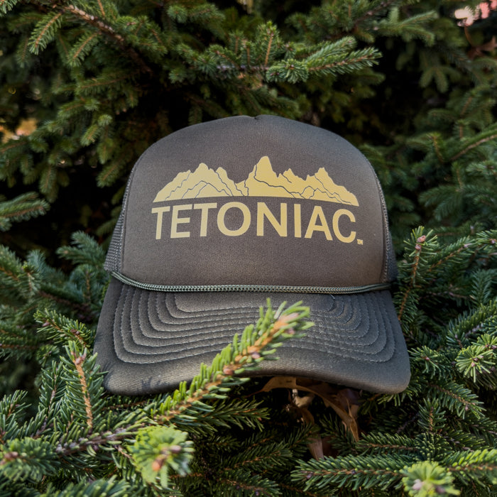 Gray cap with 'TETONIAC' logo on a background of green pine branches