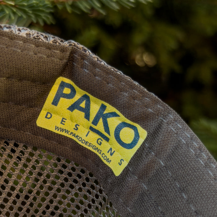 PAKO DESIGNS label on aN OLIVE  fabric background with greenery.