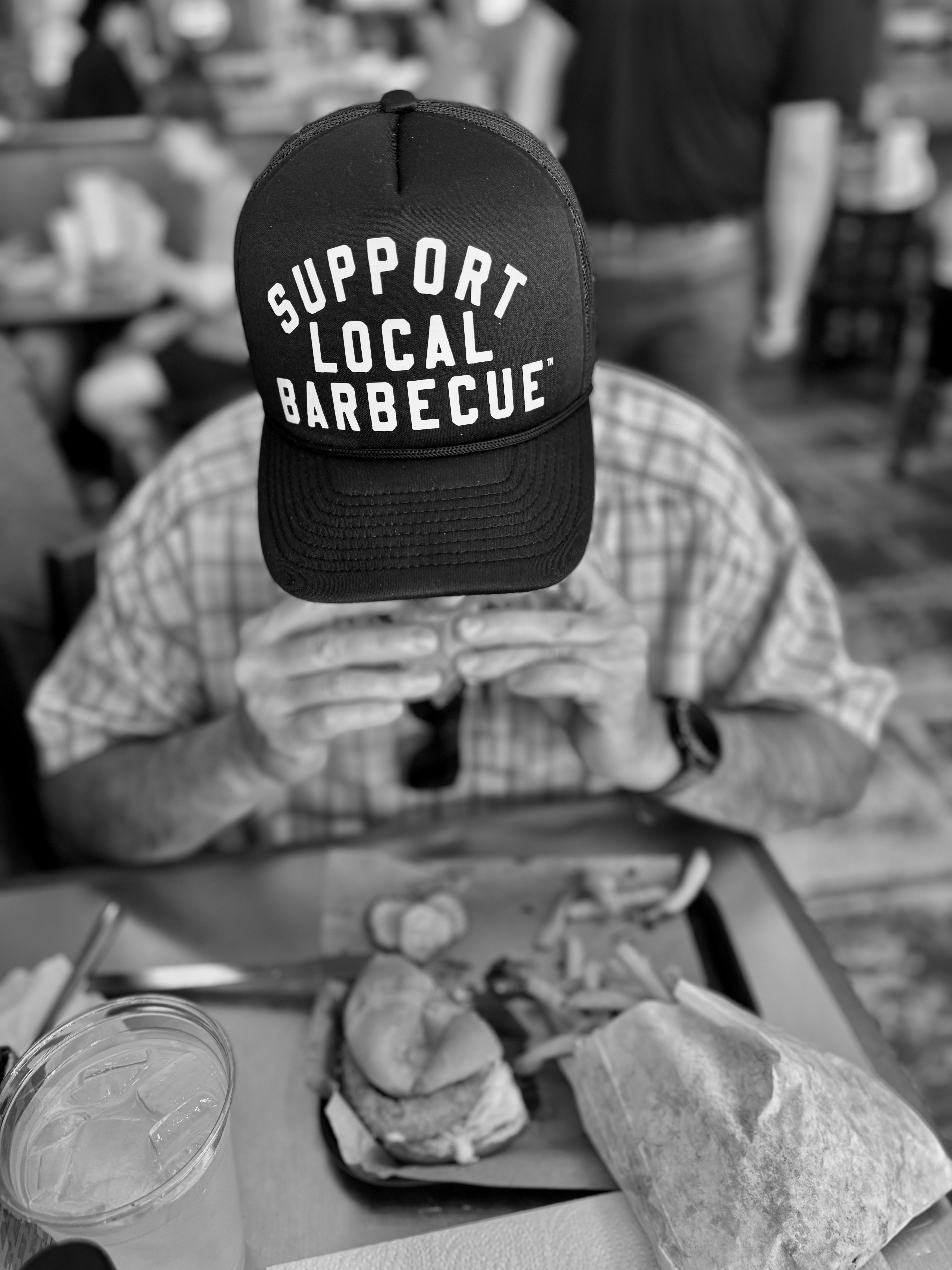 Person wearing a cap with 'Support Local Barbecue' text, sitting at a table with food.